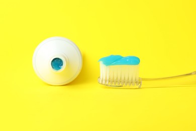 Photo of Toothbrush with toothpaste and tube on yellow background, closeup