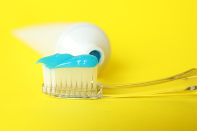 Photo of Toothbrush with toothpaste and tube on yellow background, closeup