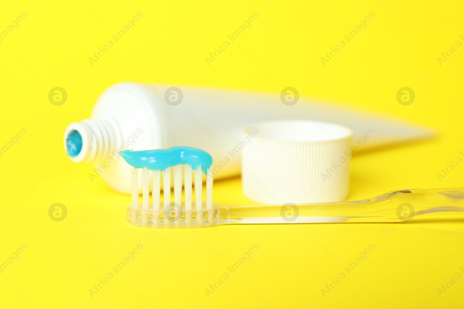 Photo of Toothbrush with toothpaste and tube on yellow background, closeup