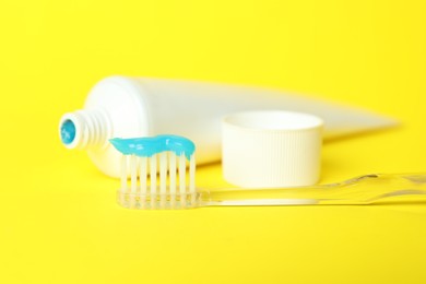 Photo of Toothbrush with toothpaste and tube on yellow background, closeup