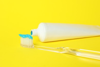 Photo of Toothbrush with toothpaste and tube on yellow background, closeup