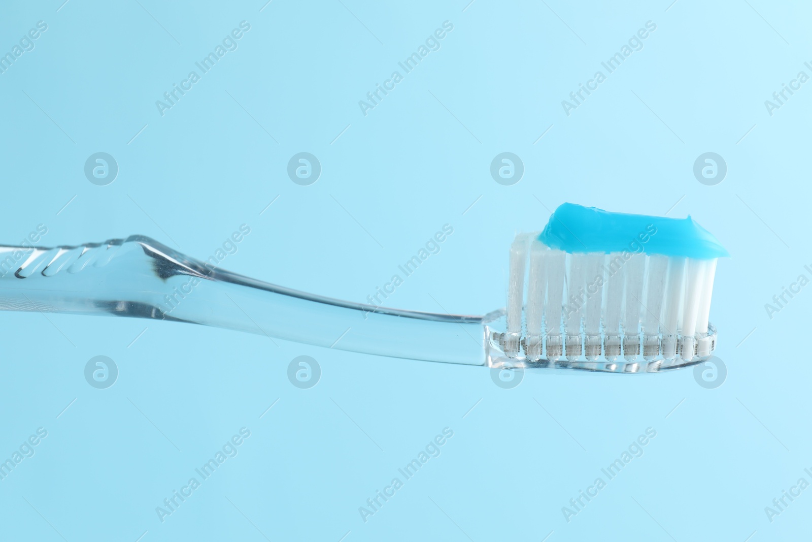 Photo of Toothbrush with toothpaste in air on light blue background, closeup