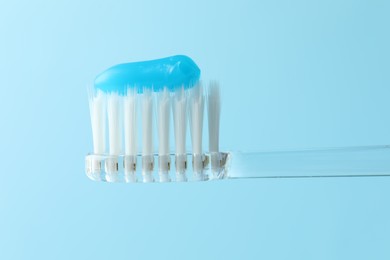 Photo of Toothbrush with toothpaste in air on light blue background, closeup