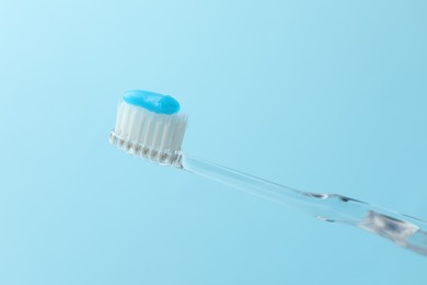 Photo of Toothbrush with toothpaste in air on light blue background, closeup