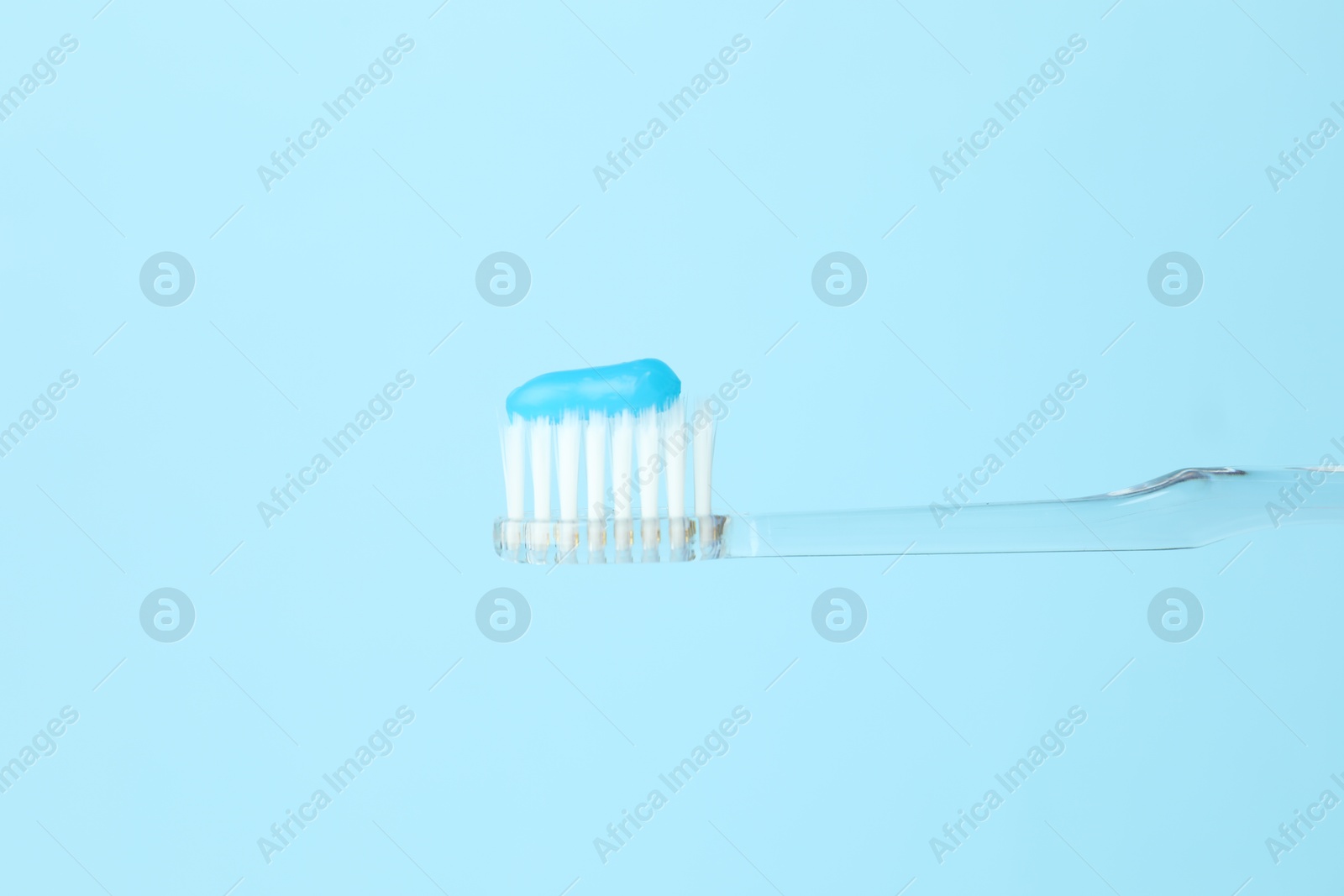 Photo of Toothbrush with toothpaste in air on light blue background, closeup. Space for text