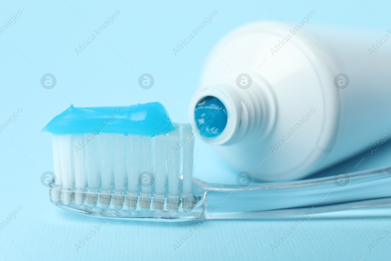 Photo of Toothbrush with toothpaste and tube on light blue background, closeup