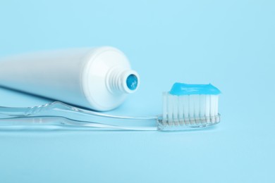 Photo of Toothbrush with toothpaste and tube on light blue background, closeup