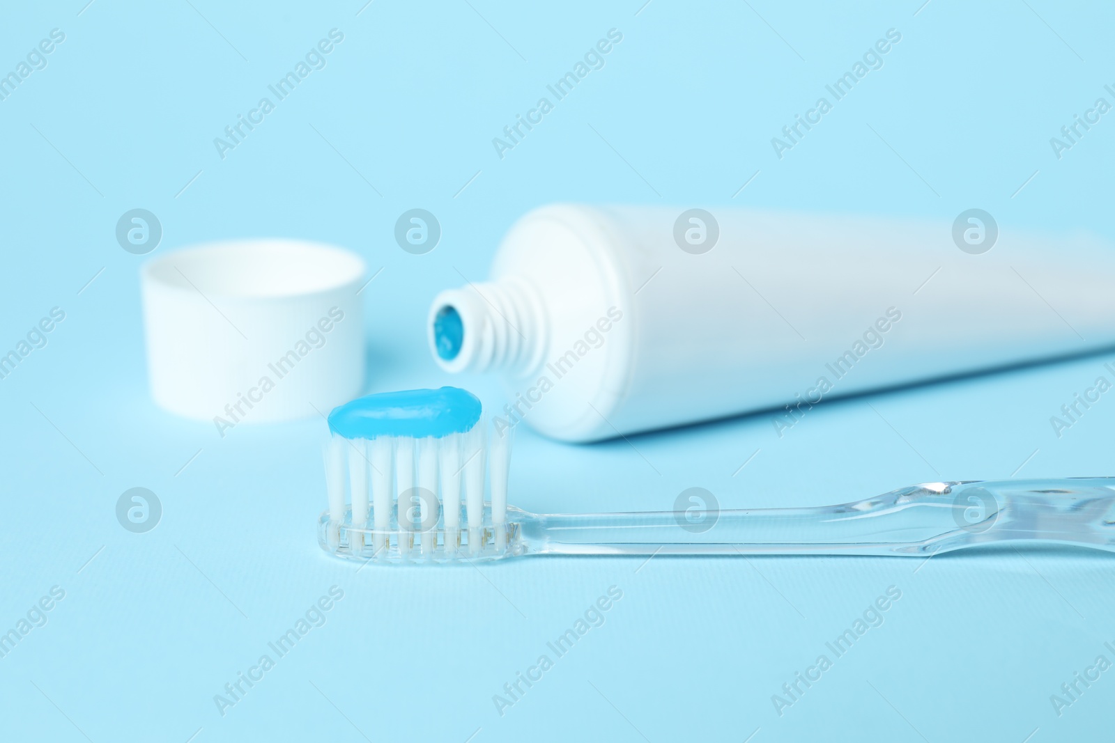 Photo of Toothbrush with toothpaste and tube on light blue background, closeup