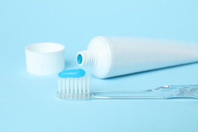 Photo of Toothbrush with toothpaste and tube on light blue background, closeup