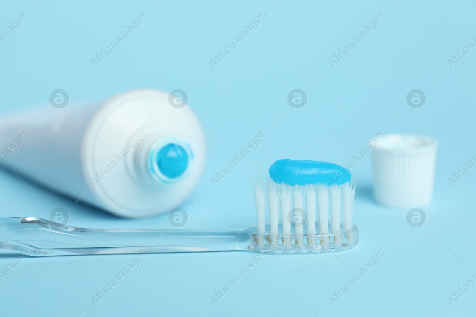 Photo of Toothbrush with toothpaste and tube on light blue background, closeup