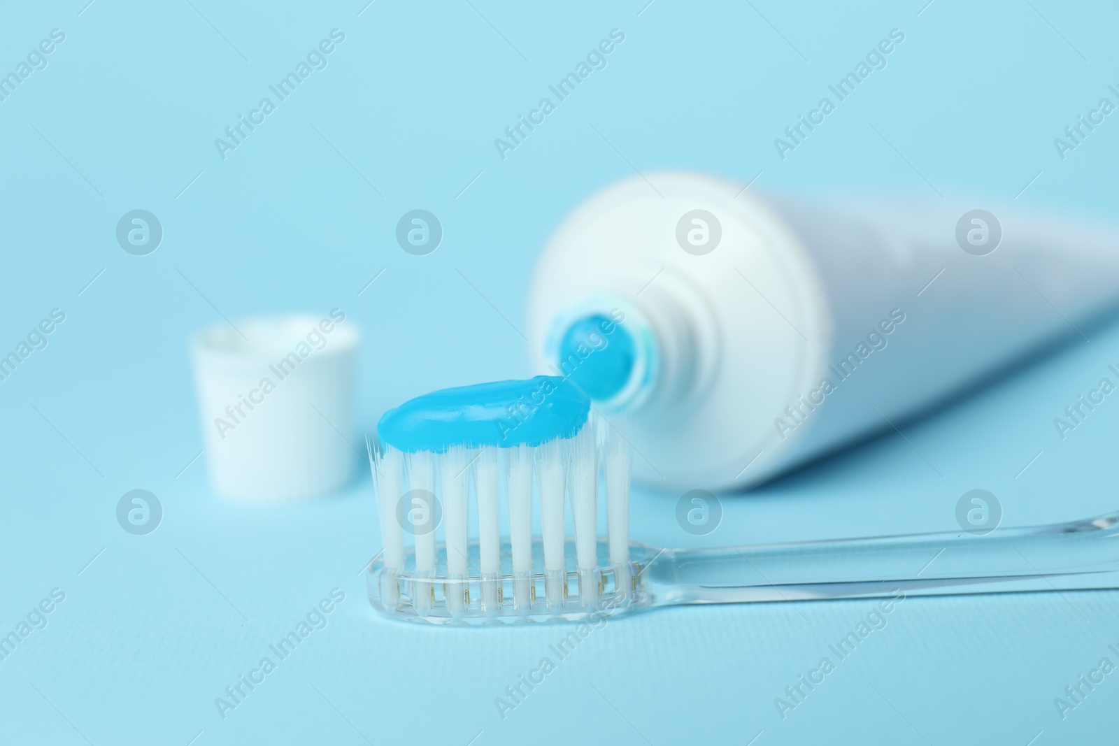 Photo of Toothbrush with toothpaste and tube on light blue background, closeup