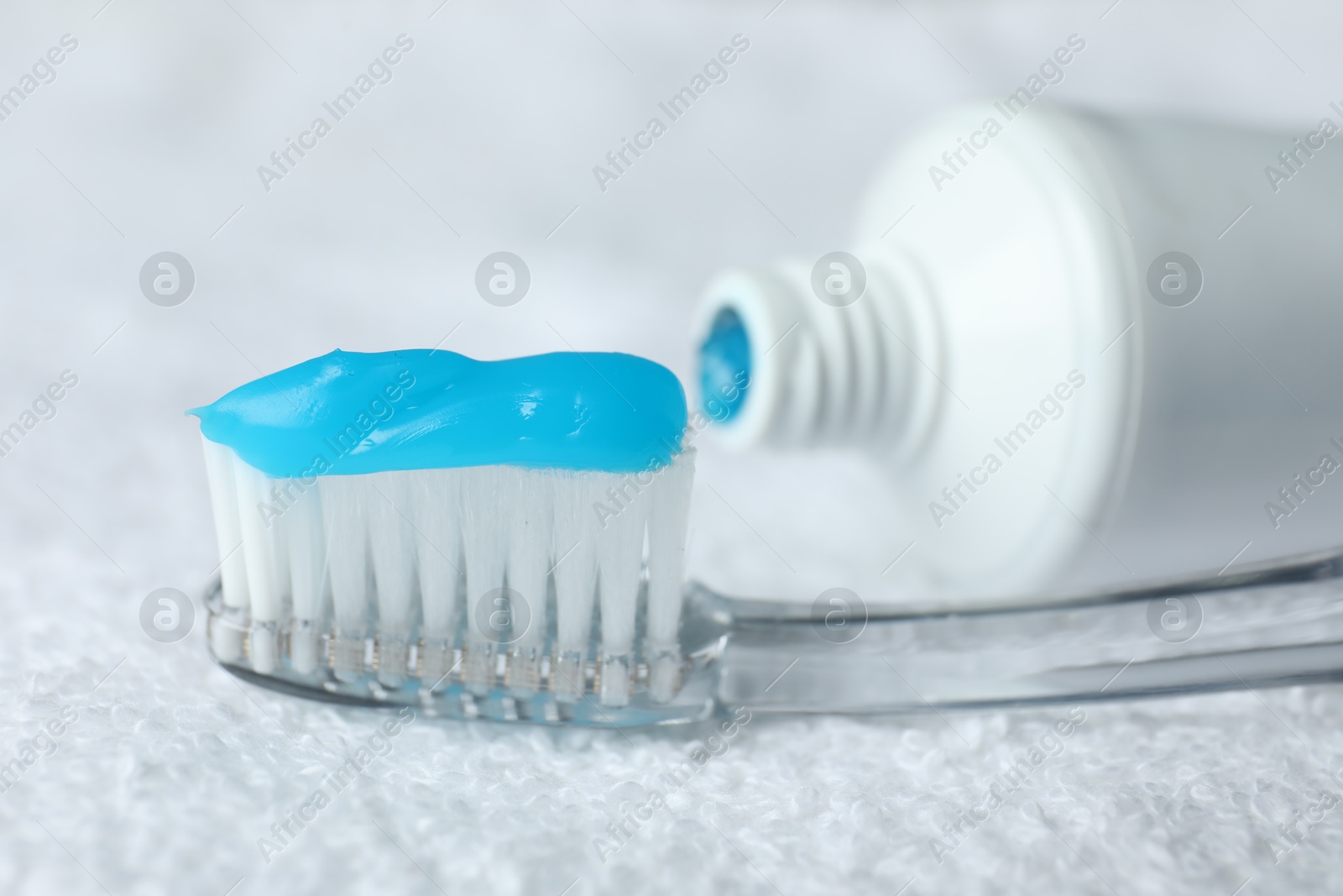 Photo of Toothbrush with toothpaste and tube on white towel, closeup