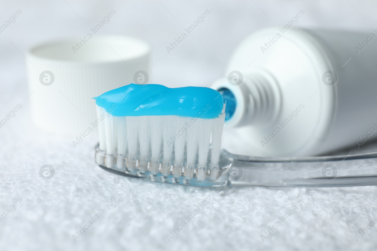 Photo of Toothbrush with toothpaste and tube on white towel, closeup