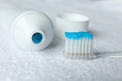 Photo of Toothbrush with toothpaste and tube on white towel, closeup