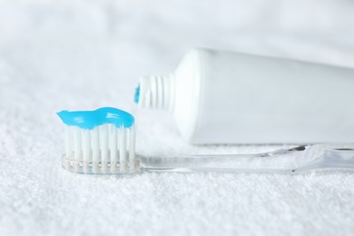 Photo of Toothbrush with toothpaste and tube on white towel, closeup