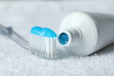 Photo of Toothbrush with toothpaste and tube on white towel, closeup