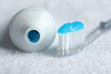 Photo of Toothbrush with toothpaste and tube on white towel, closeup