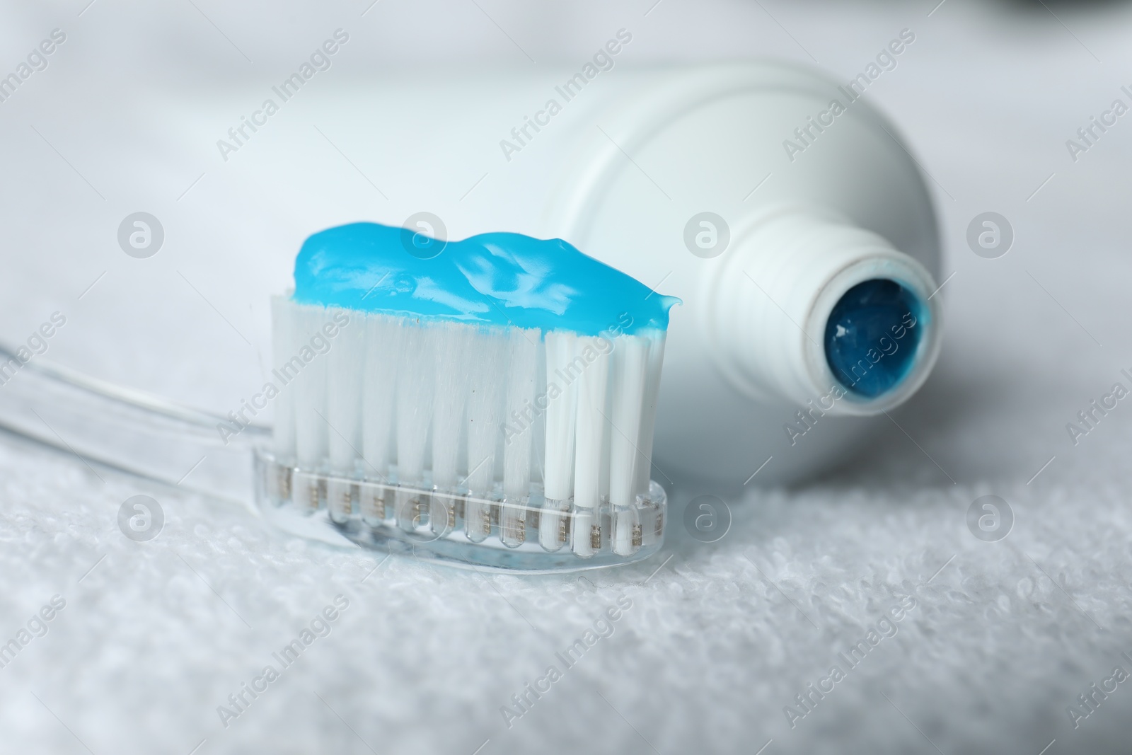 Photo of Toothbrush with toothpaste and tube on white towel, closeup