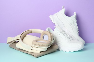 Photo of Pair of stylish white sneakers, sportswear and headphones on color background