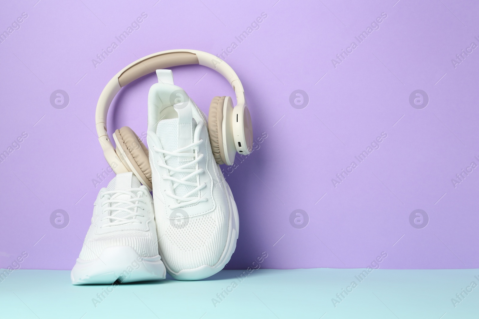 Photo of Pair of stylish white sneakers and headphones on color background, space for text