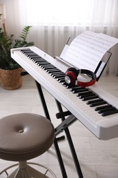 Photo of Synthesizer with music sheets, headphones and stool indoors