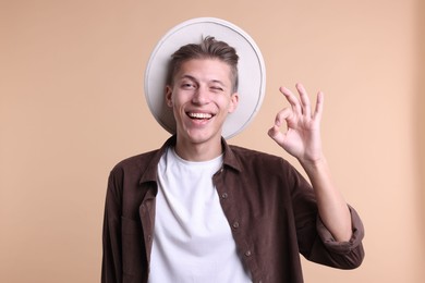 Photo of Happy young man showing OK gesture on beige background