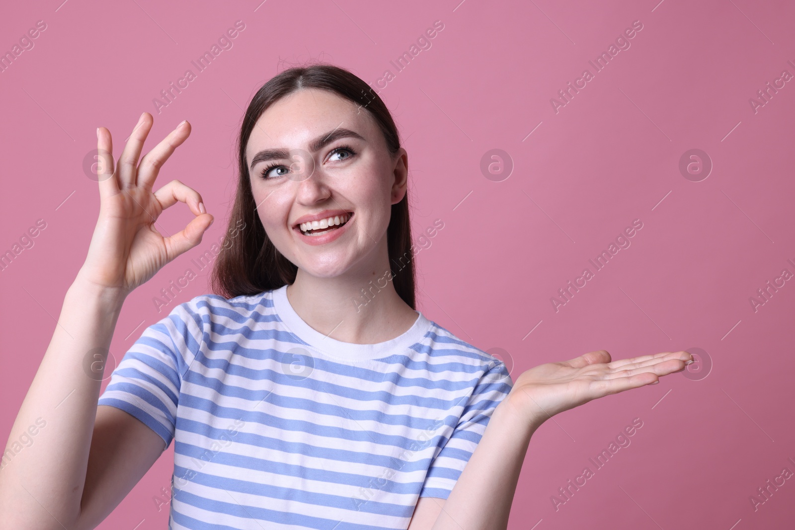 Photo of Happy young woman showing OK gesture on pink background, space for text