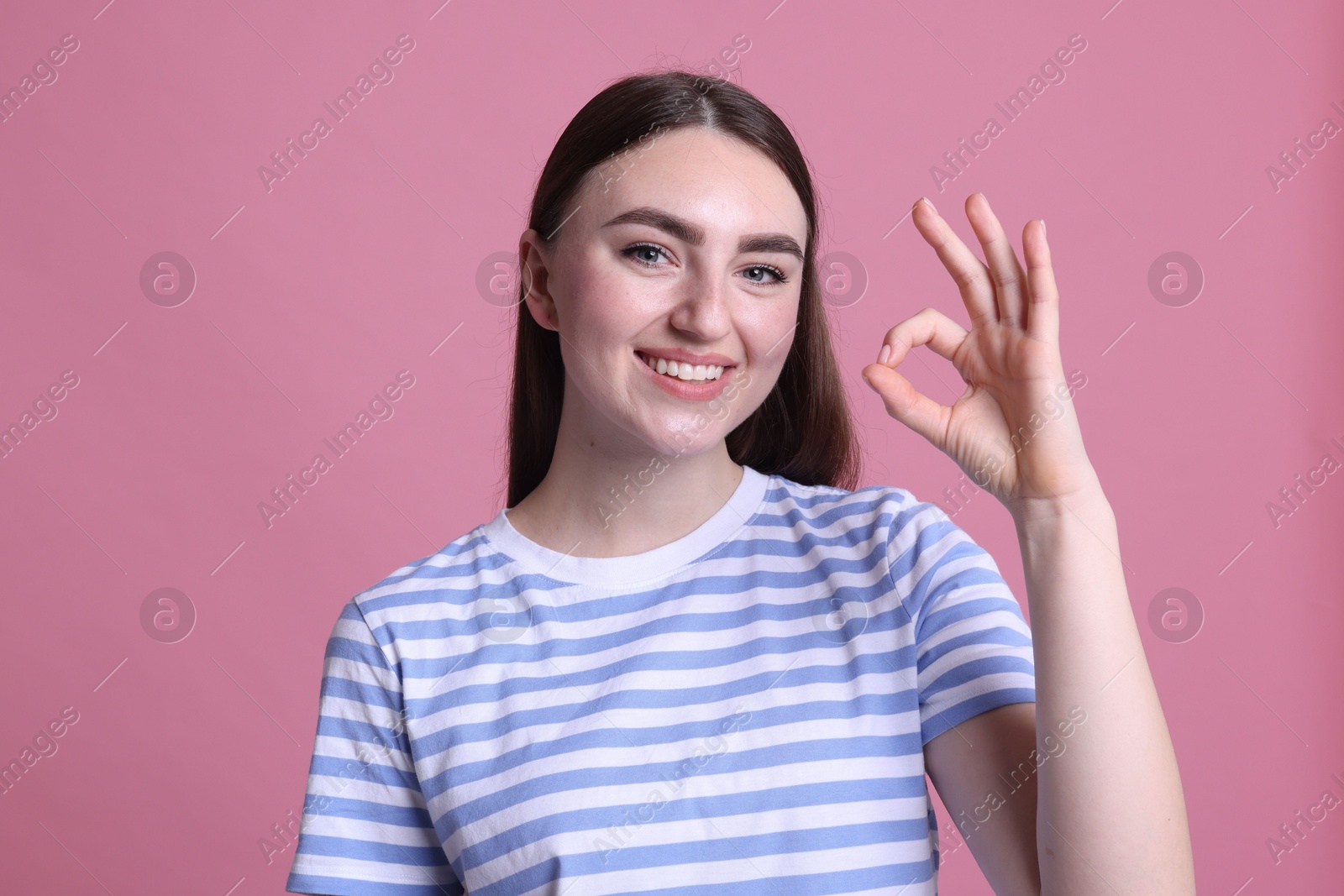 Photo of Happy young woman showing OK gesture on pink background