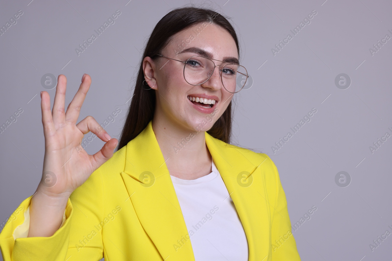 Photo of Happy young woman showing OK gesture on gray background, space for text