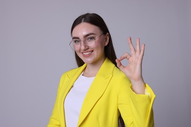 Happy young woman showing OK gesture on gray background