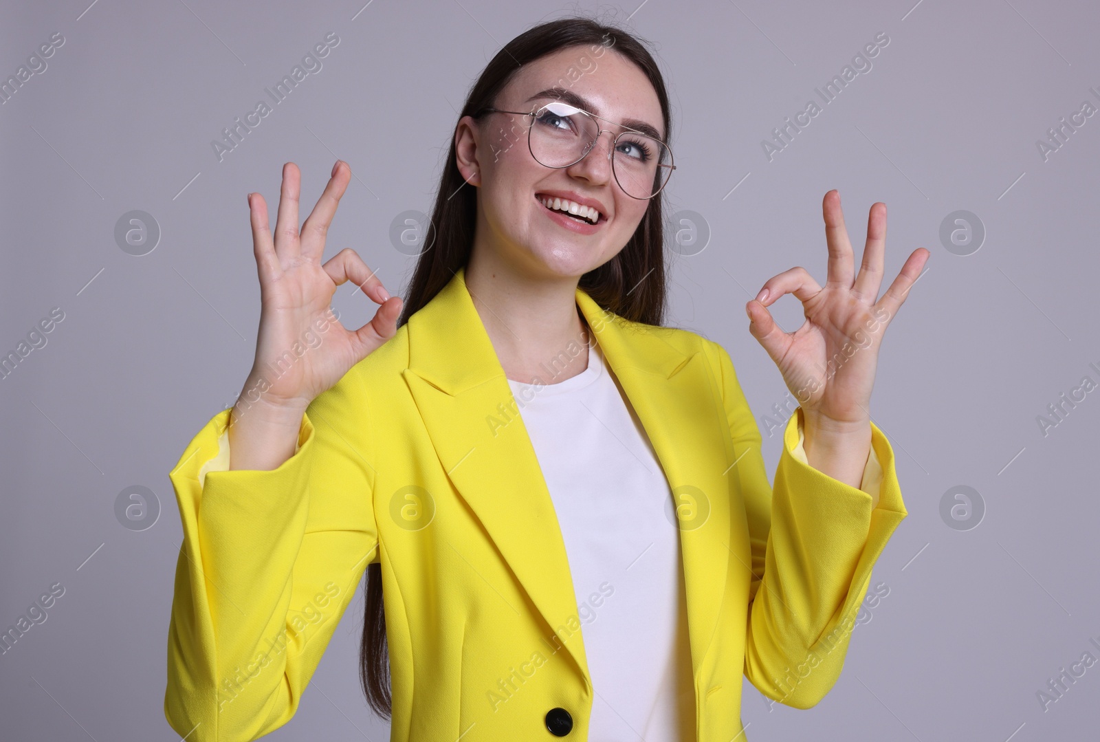 Photo of Happy young woman showing OK gesture on gray background