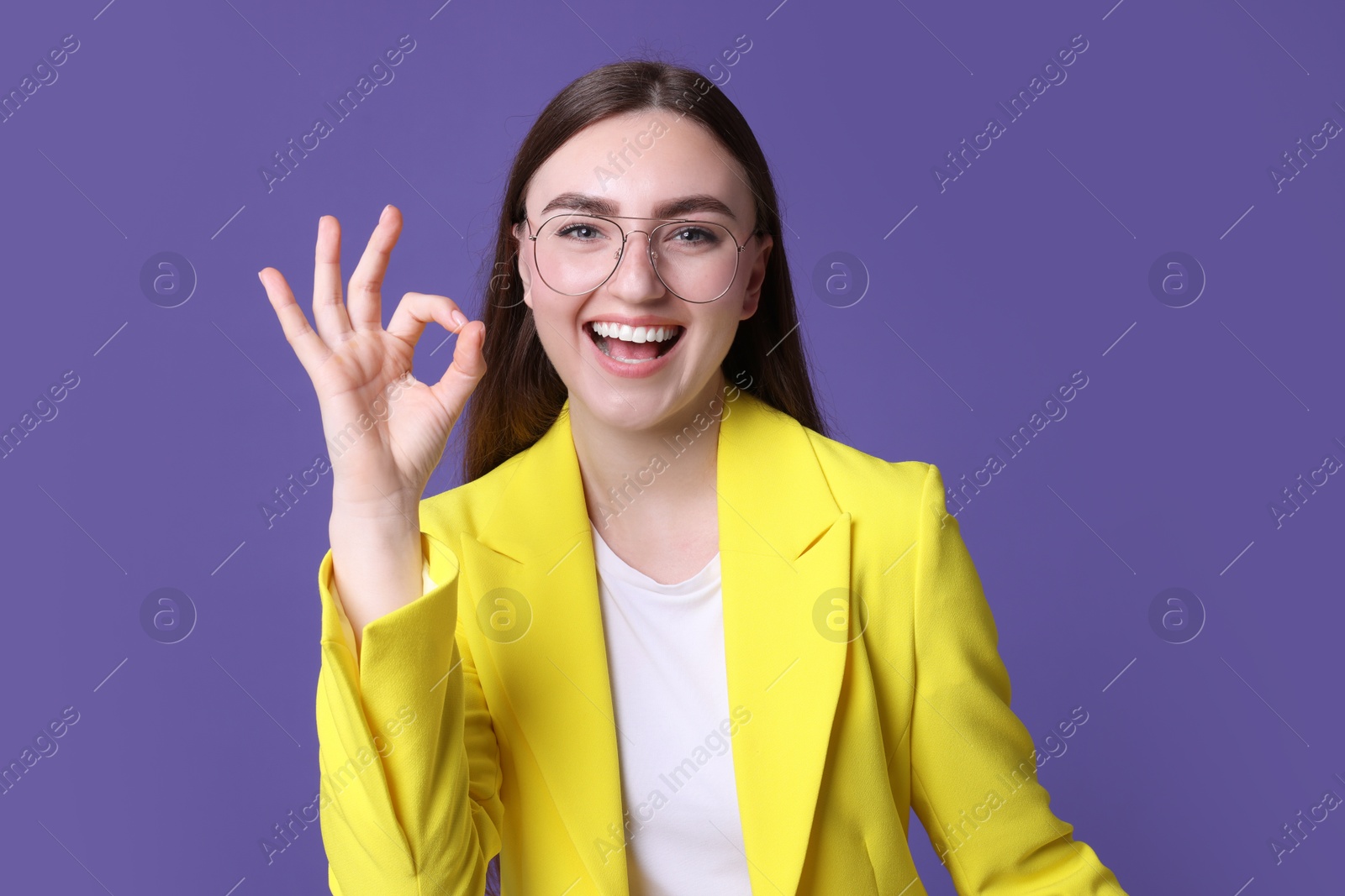 Photo of Happy young woman showing OK gesture on violet background