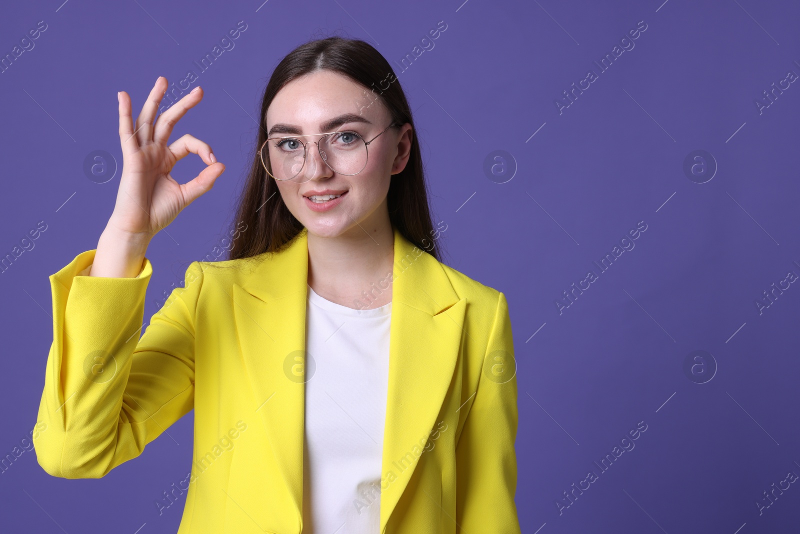 Photo of Beautiful young woman showing OK gesture on violet background, space for text