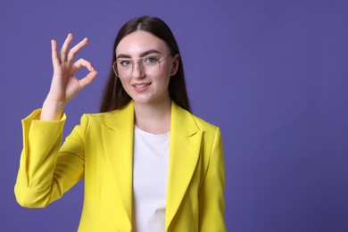 Beautiful young woman showing OK gesture on violet background, space for text