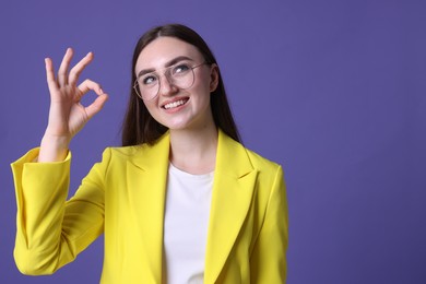 Photo of Happy young woman showing OK gesture on violet background, space for text