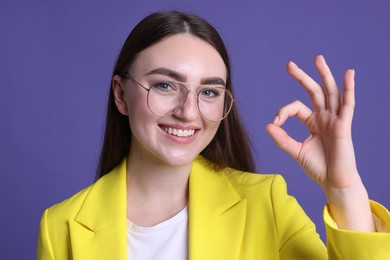 Photo of Happy young woman showing OK gesture on violet background