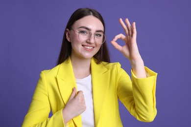 Photo of Happy young woman showing OK gesture on violet background