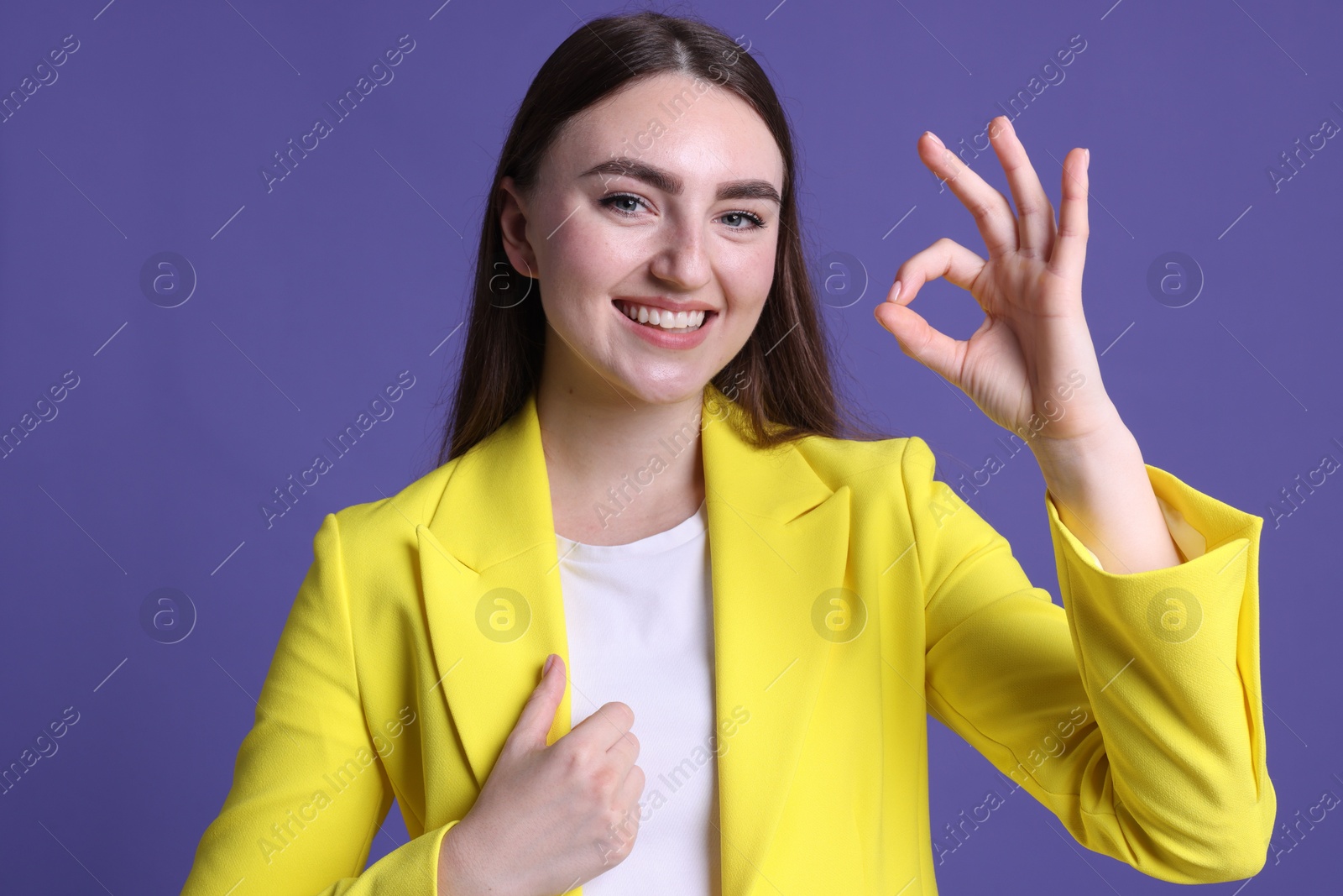 Photo of Happy young woman showing OK gesture on violet background