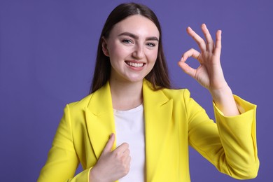 Photo of Happy young woman showing OK gesture on violet background