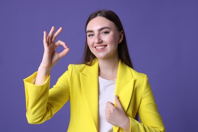 Photo of Happy young woman showing OK gesture on violet background