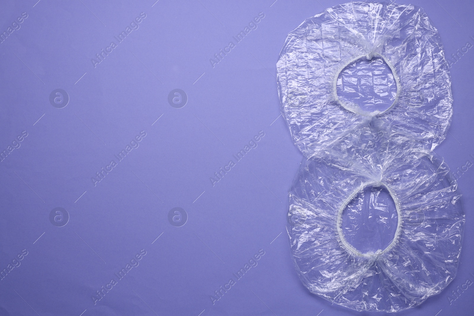 Photo of Two shower caps on violet background, flat lay. Space for text