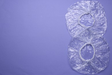 Photo of Two shower caps on violet background, flat lay. Space for text