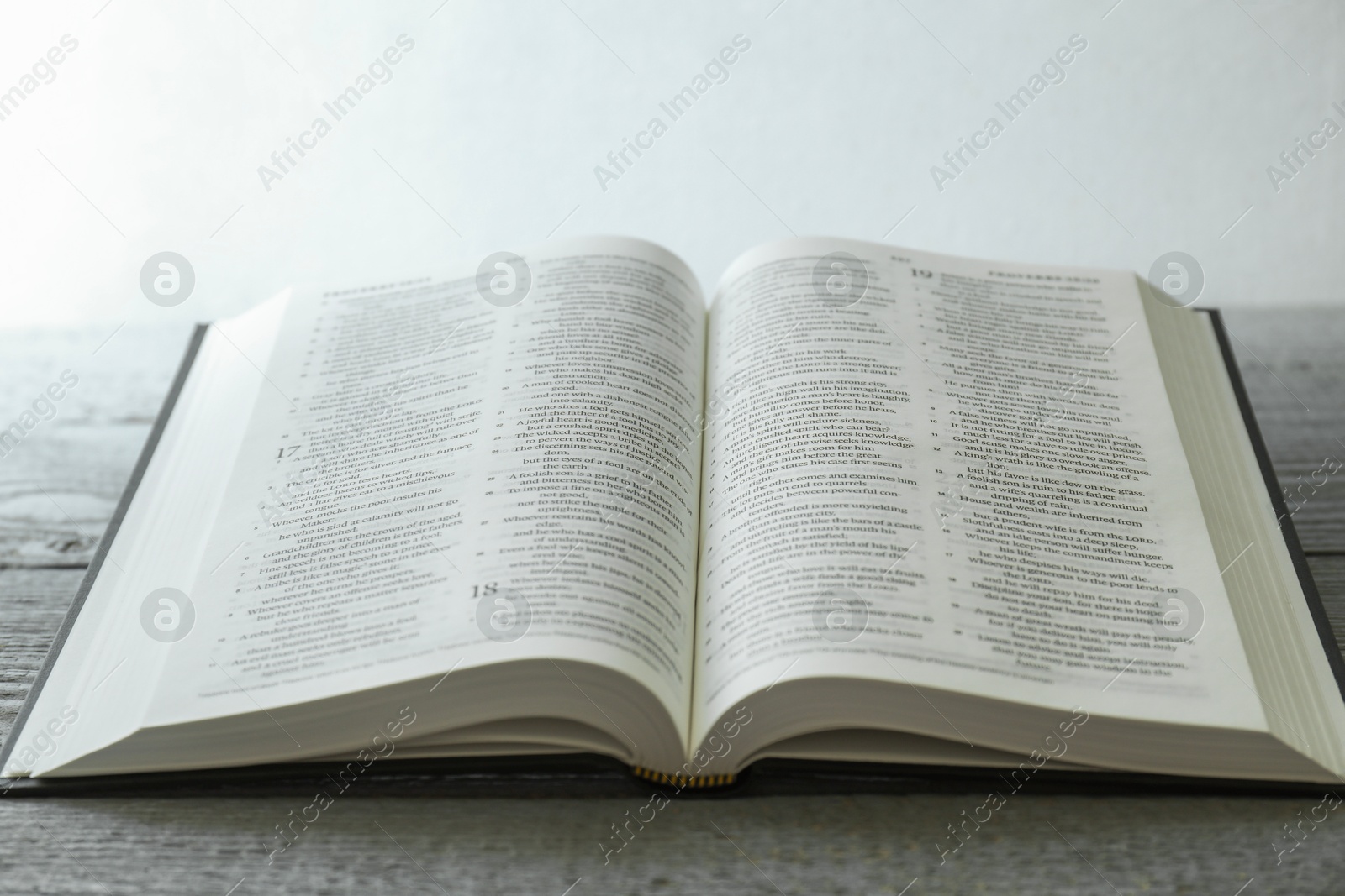 Photo of Open Holy Bible in English language on wooden table, closeup