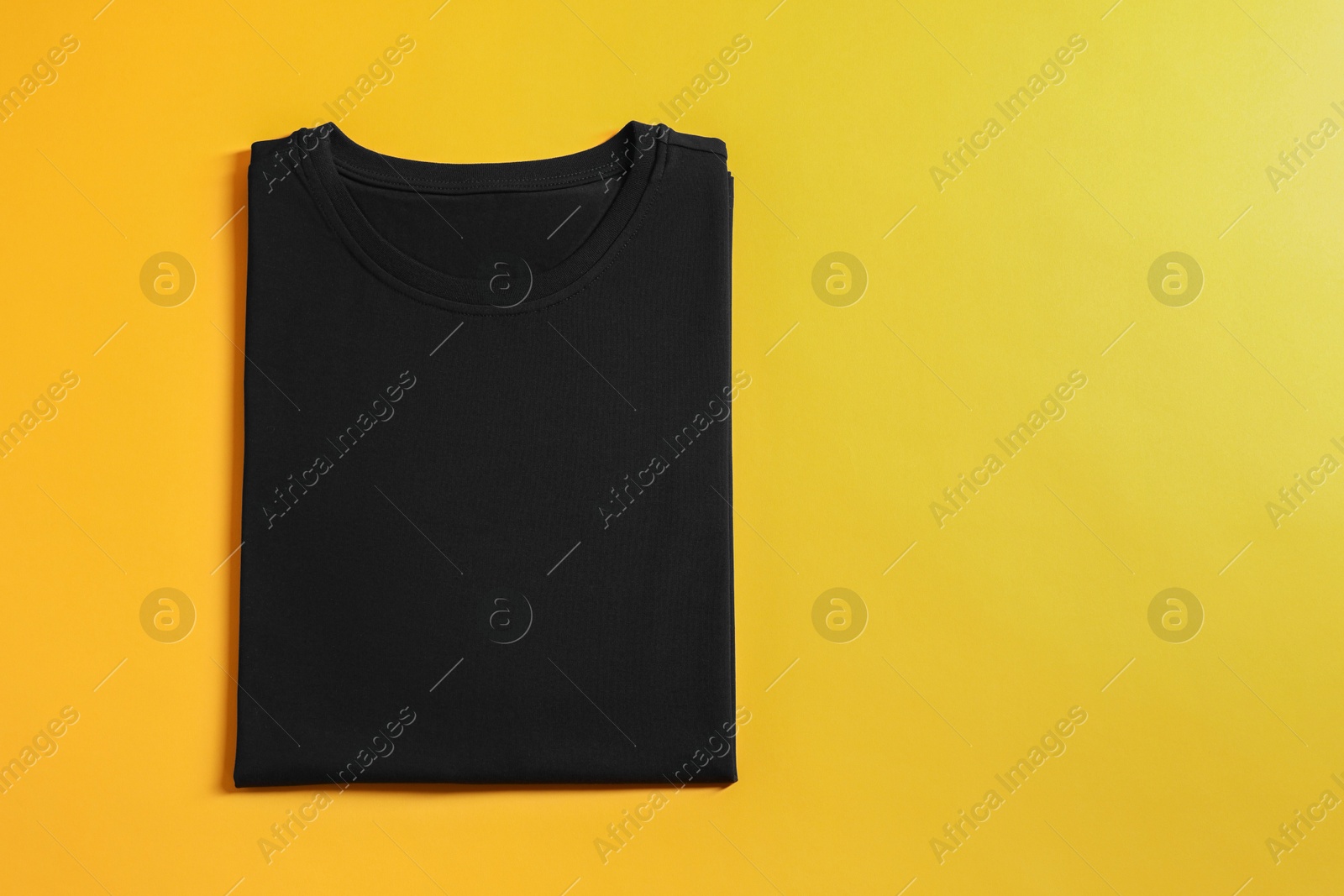 Photo of Blank black t-shirt on yellow background, top view. Mockup for design