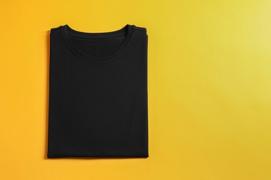 Photo of Blank black t-shirt on yellow background, top view. Mockup for design