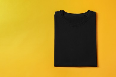 Photo of Blank black t-shirt on yellow background, top view. Mockup for design