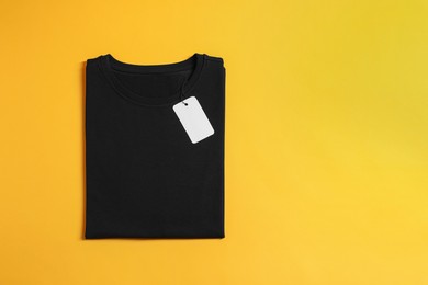 Photo of Blank black t-shirt on yellow background, top view. Mockup for design