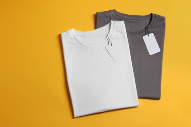 Photo of Different blank t-shirts on yellow background, top view. Mockup for design