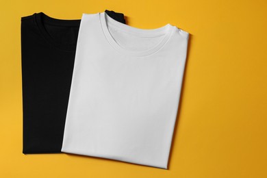 Photo of Different blank t-shirts on yellow background, top view. Mockup for design