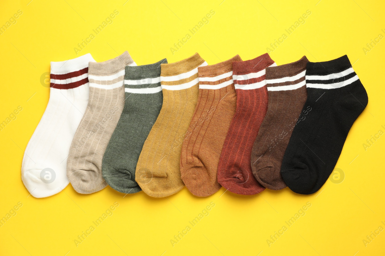 Photo of Different soft socks on yellow background, flat lay